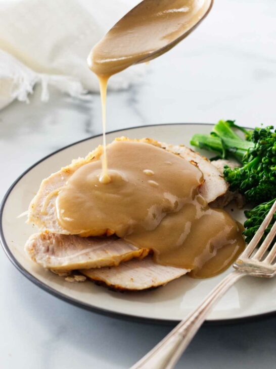 Drizzling gravy over slices of turkey on a plate.