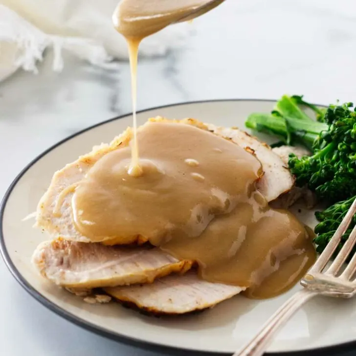 Drizzling gravy over slices of turkey on a plate.