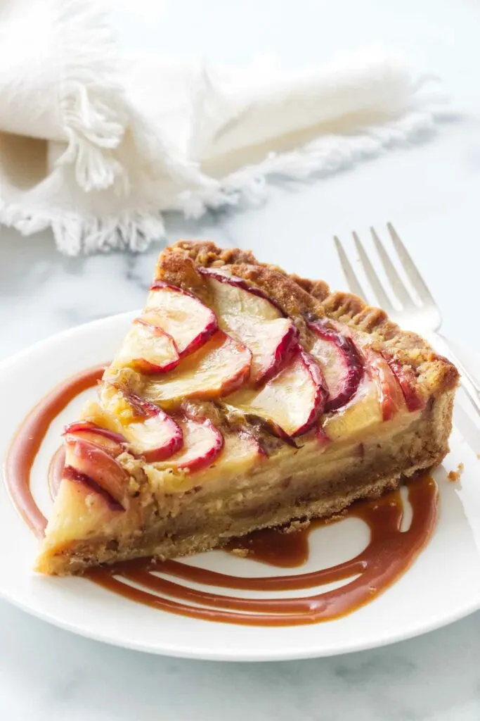 A slice of apple frangipane tart on a plate with butterscotch sauce.