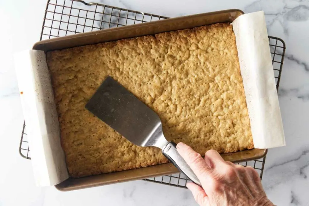 Shortbread cookie base with a spatula pressing it down.
