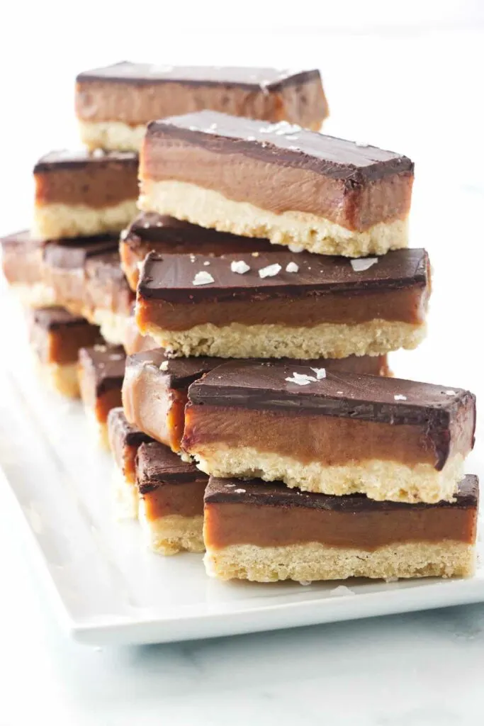 A plate stacked with 3-layer Billionaire Bar cookies.