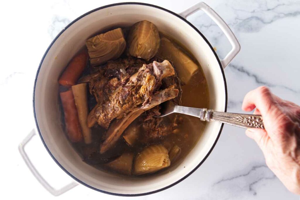 Removing beef and bones from a soup pot with vegetables and broth.