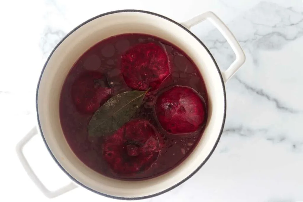 Four red beets and bay leaves in a soup pot.