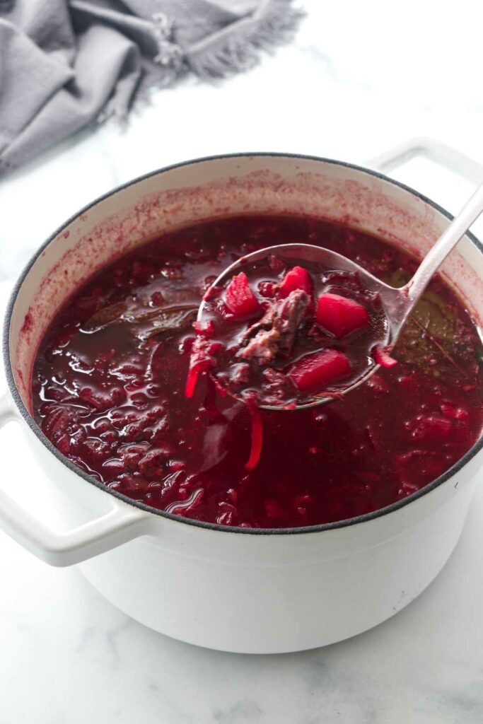 A soup pot filled with borscht and a ladle lifting a scoop of soup.