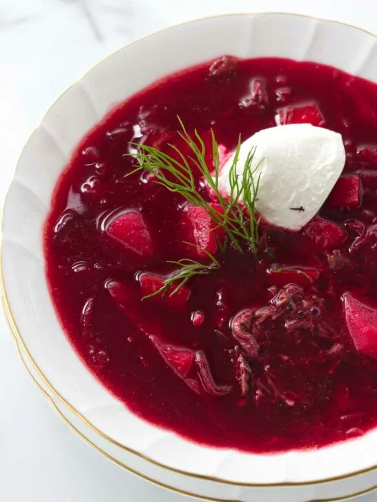 A soup bowl of borscht garnished with sour cream and a sprig of dill.
