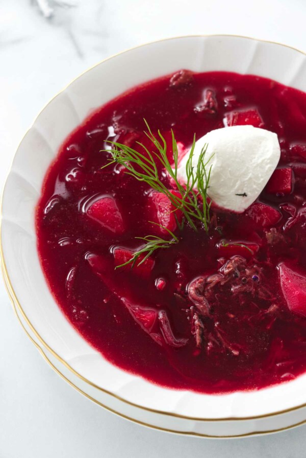 A soup bowl of borscht garnished with sour cream and a sprig of dill.