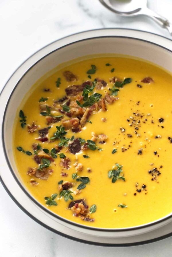 Butternut soup garnished with bacon bits, thyme leaves and ground pepper.