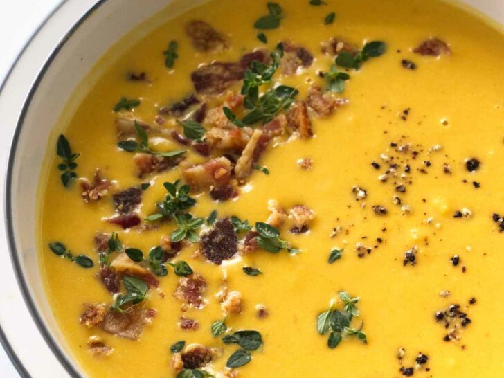 Butternut soup garnished with bacon bits, thyme leaves and ground pepper.