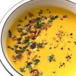 Butternut soup garnished with bacon bits, thyme leaves and ground pepper.