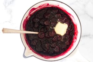 A saucepan with cherry compote; butter on top.