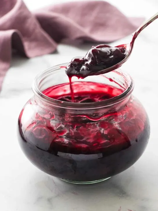 serving spoon scooping up cherry sauce from the jar of sauce.