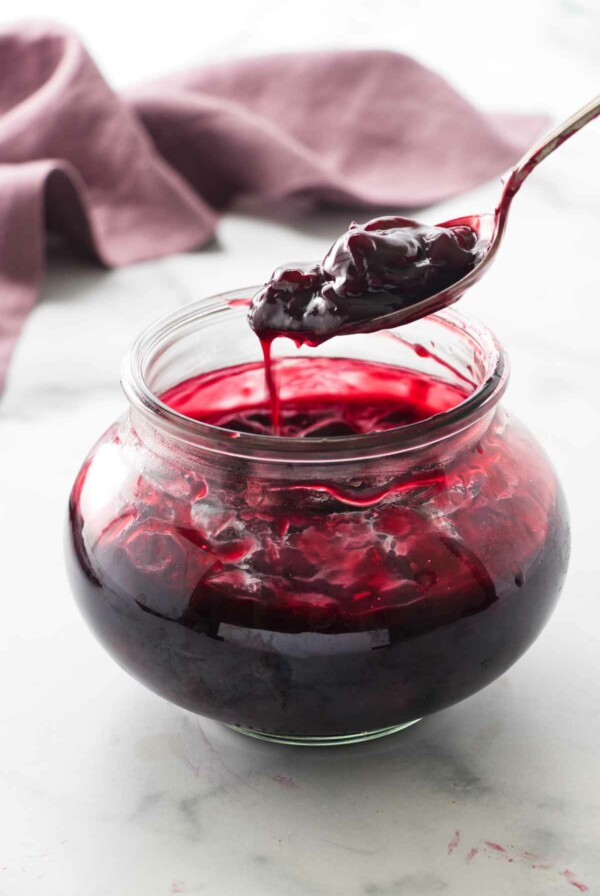 serving spoon scooping up cherry sauce from the jar of sauce.