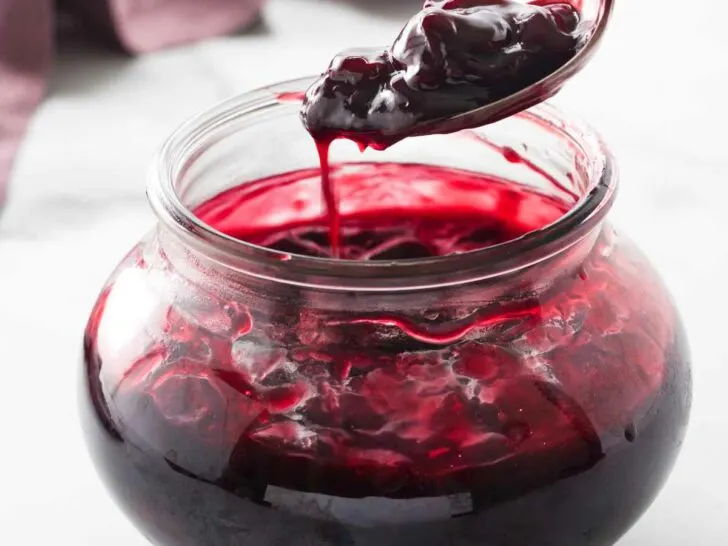 serving spoon scooping up cherry sauce from the jar of sauce.