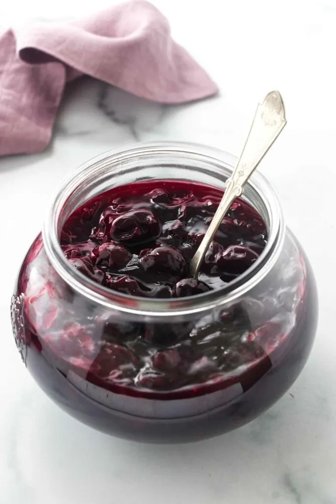 A jar filled with cherry sauce and a spoon.