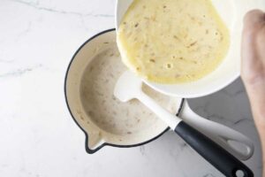 Pouring the tempered egg mixture into the saucepan.