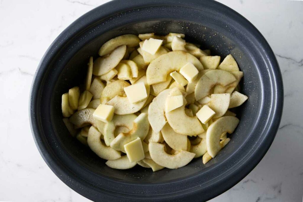 Apple slices in a crock pot topped with cubes of butter.