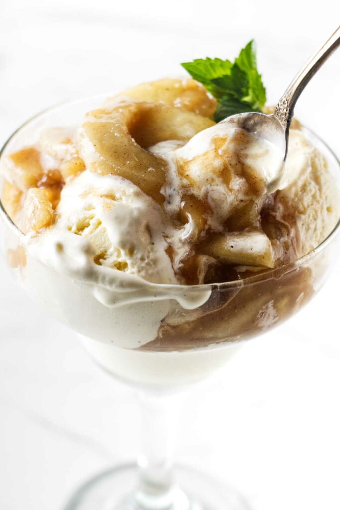 Spiced apple pie filling on top of ice cream in a glass bowl.