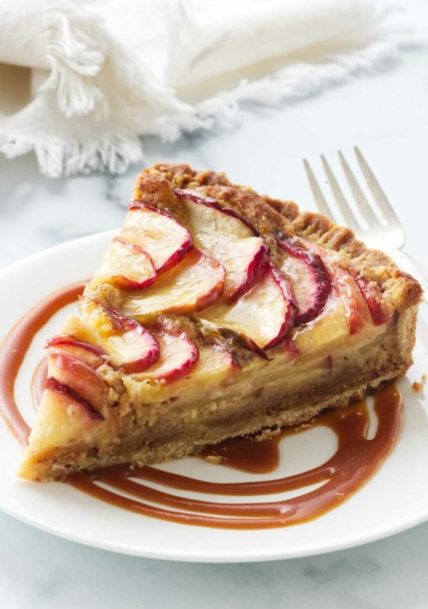 A slice of apple frangipane tart on a plate with butterscotch sauce.