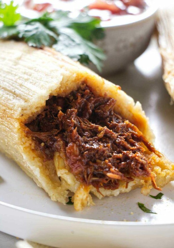 A pork tamale on a plate next to salsa.