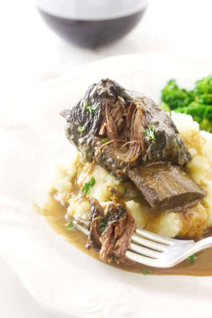 A fork shredding a beef rib on a bed of mashed potatoes.