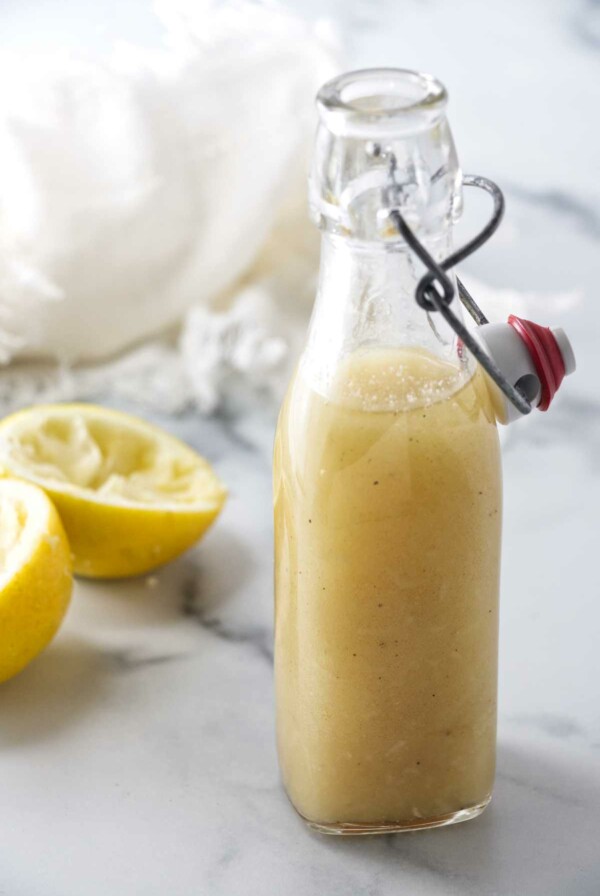 An opened bottle of salad dressing, two lemon rinds and a napkin in the background.