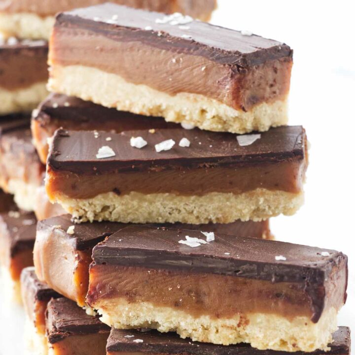 A stack of cookie bars, a layer of shortbread, a layer of caramel and a layer of chocolate ganache with salt flakes sprinkled on top.