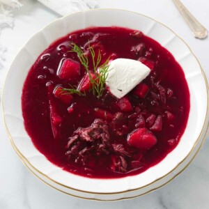 A soup bowl of borscht garnished with sour cream and a sprig of dill.