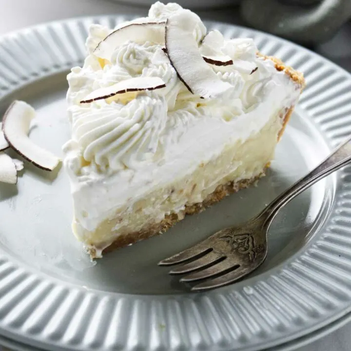 A slice of coconut cream pie on a plate with a fork.