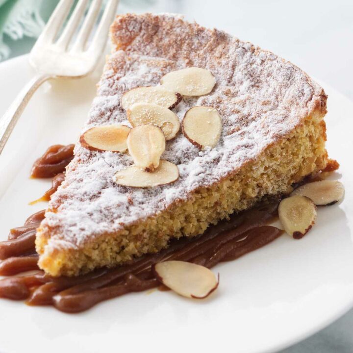 Salted caramel on a plate with a slice of almond cake garnished with sliced almonds.