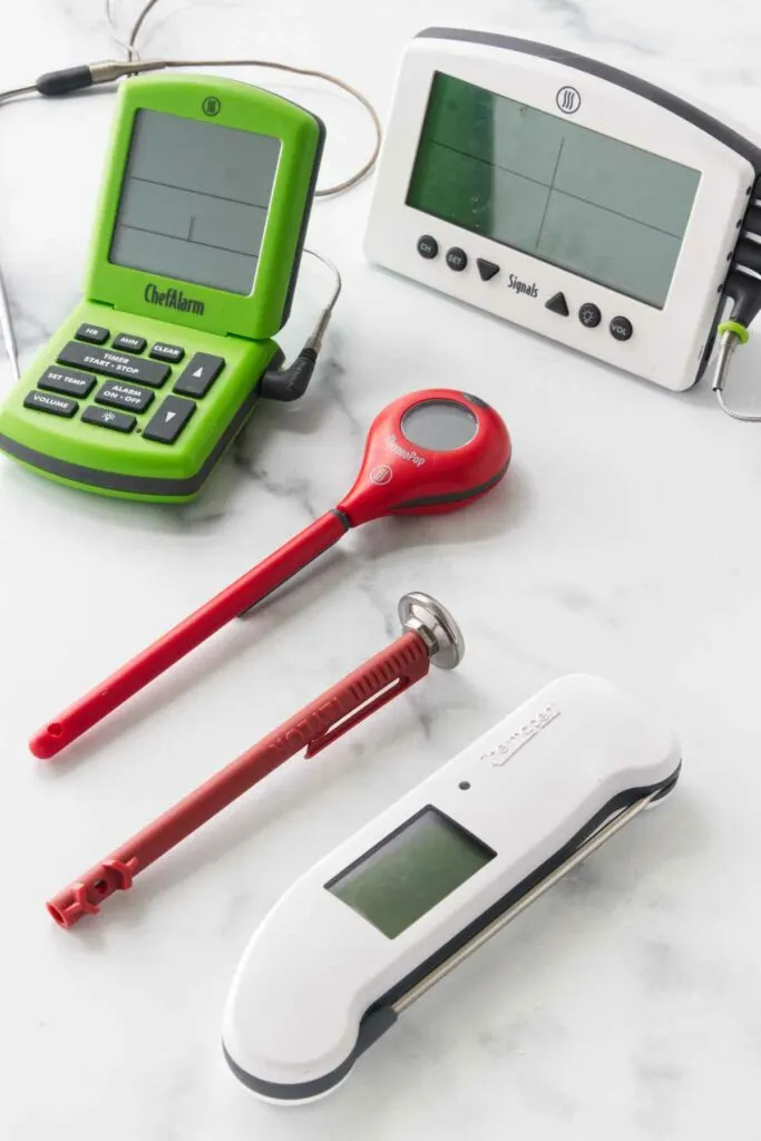 Five different kinds of meat thermometers on a white countertop.