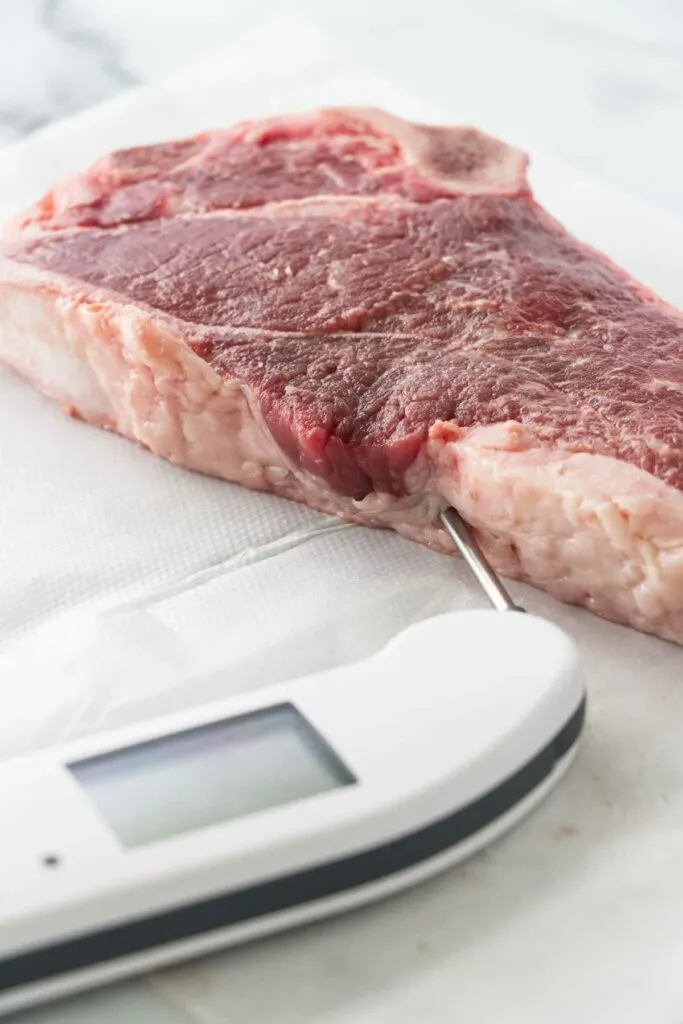 Inserting a meat thermometer in a raw steak.