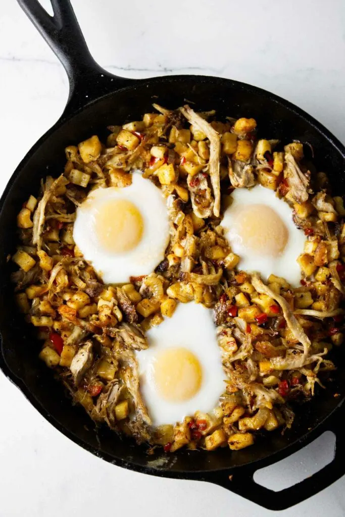 Pork and potato hash in a skillet with eggs on top.