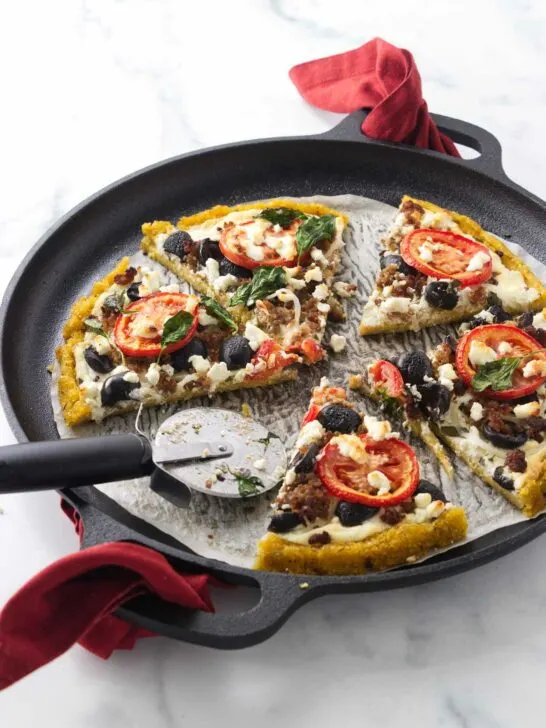 A cornmeal crust pizza on a parchment-lined pizza pan with a pizza cutter.