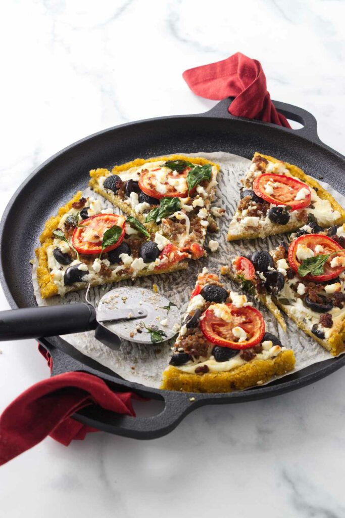 A cornmeal crust pizza on a parchment-lined pizza pan with a pizza cutter.