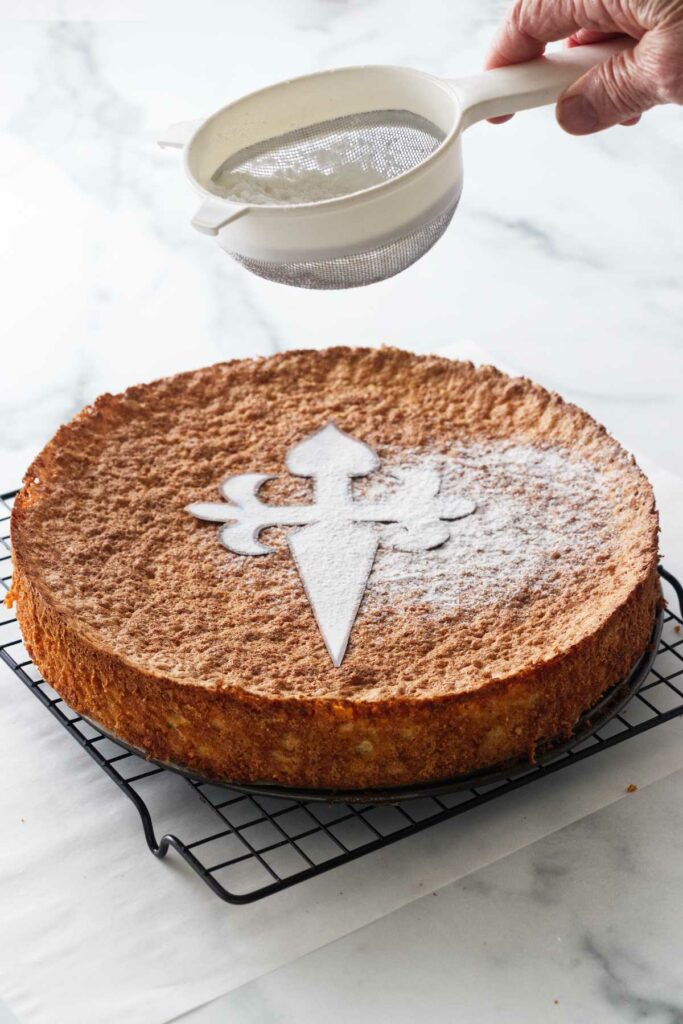Baked Spanish almond cake with a stencil on top and confectioners' sugar being dusted over the top.