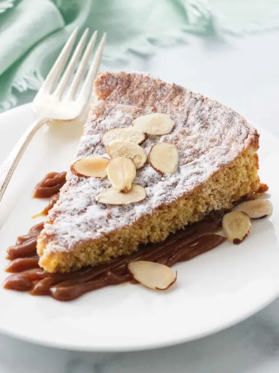 A serving of almond cake on a plate with salted caramel and sliced almonds.