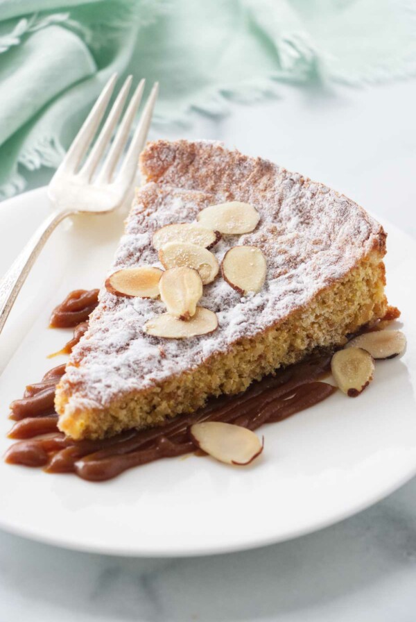 A serving of almond cake on a plate with salted caramel and sliced almonds.