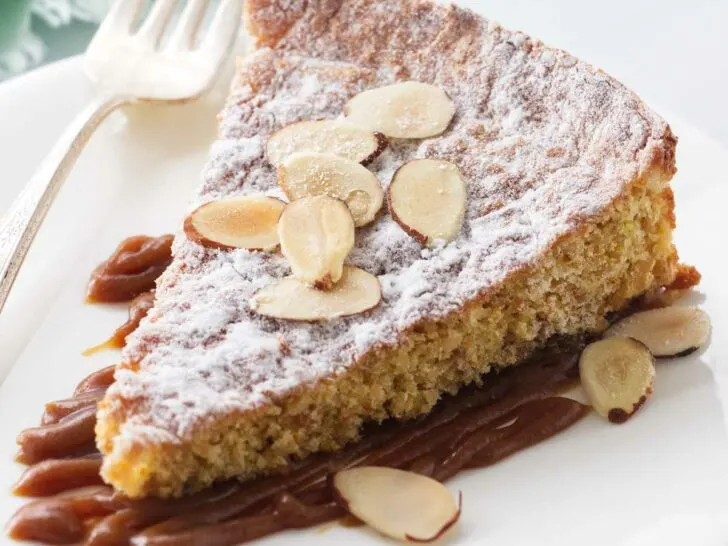 A serving of almond cake on a plate with salted caramel and sliced almonds.