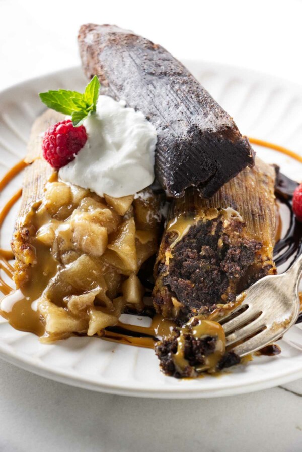 Three sweet tamales on a dessert plate with whipped cream and dulce de leche.