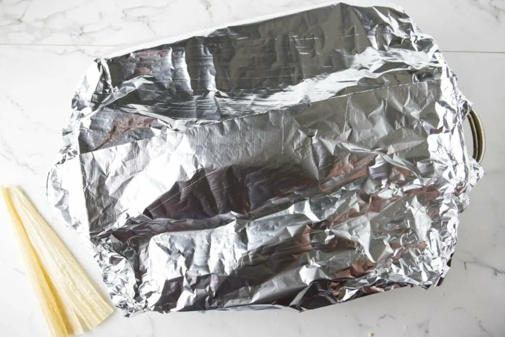 Covering a roasting pan with aluminum foil to hold steam in while tamales bake.