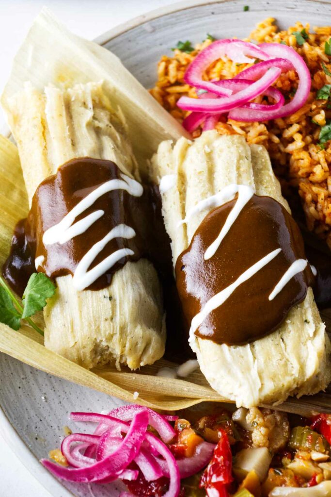 Two tamales on a plate next to pickled onions and rice.