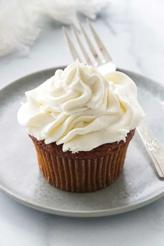 A serving of cupcake covered with frosting on a plate with a fork.