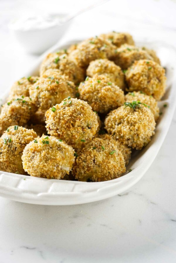 A serving tray of loaded potato croquettes next to a dish of sour cream.