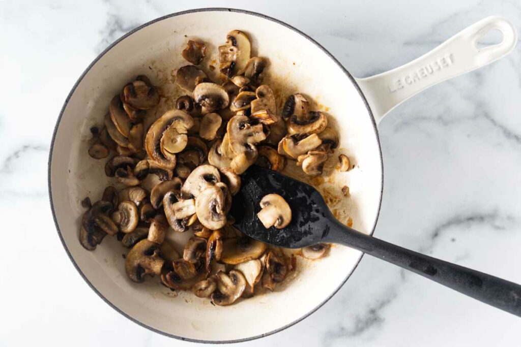 A skillet with sauteed mushrooms and a black silicone spatula.
