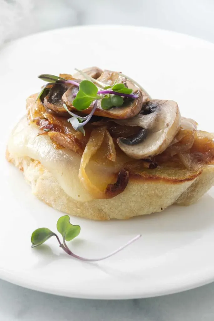 A small plate with a bruschetta appetizer serving of caramelized onions, mushrooms and cheese. Garnished with microgreens.