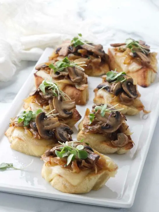 small appetizers of bread, cheese, onions and mushrooms on a plate.
