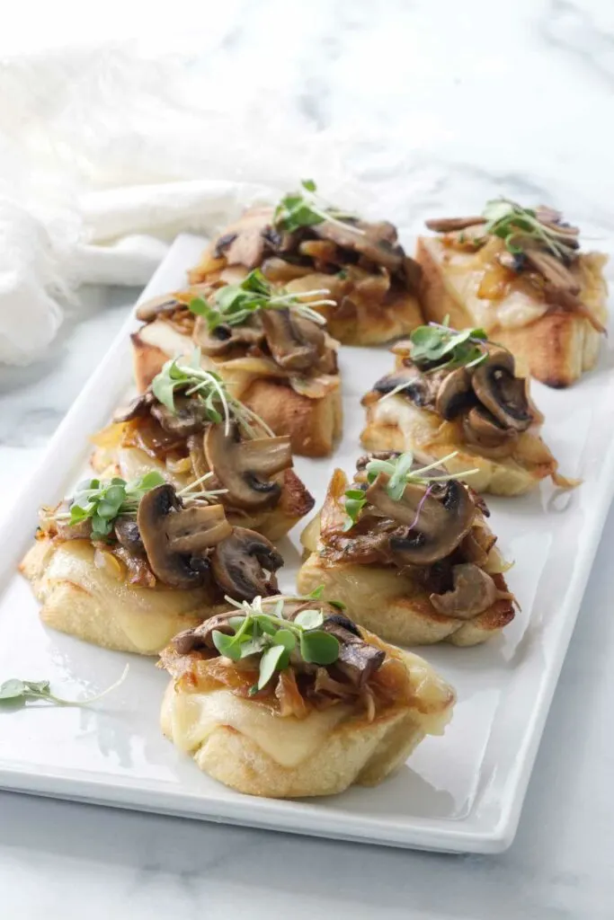 small appetizers of bread, cheese, onions and mushrooms on a plate.