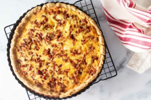 Baked quiche on a cooling rack with kitchen towel in the upper right.corner.