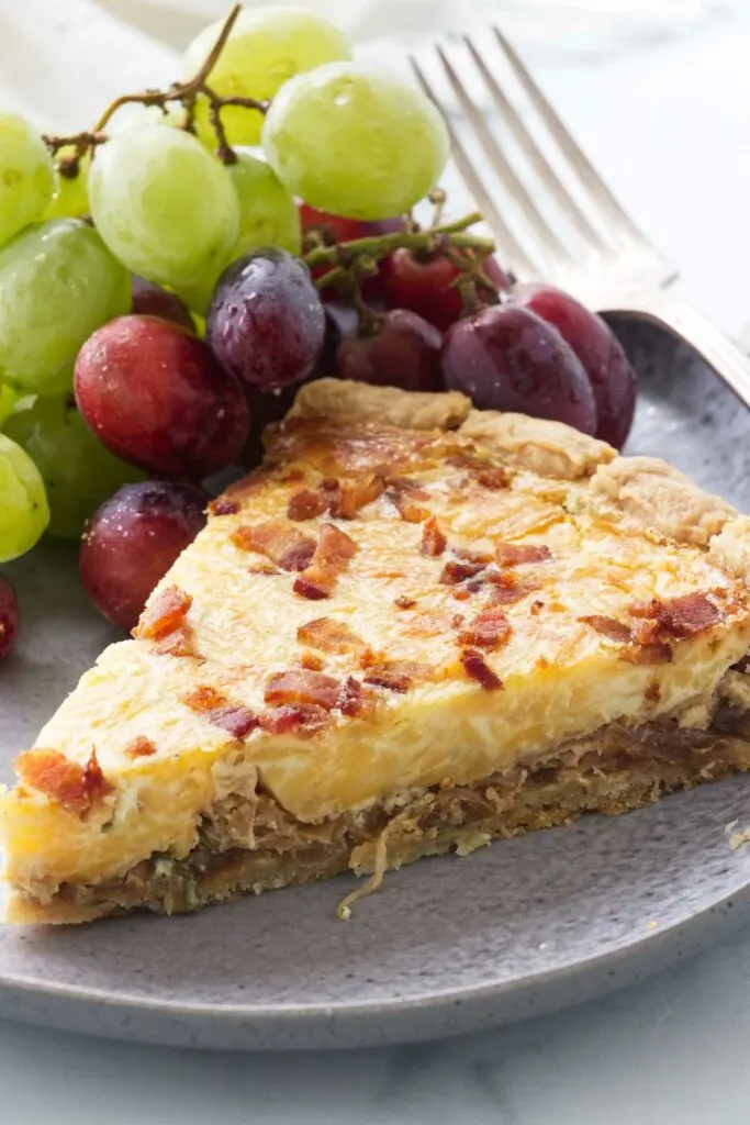 A serving of onion quiche on a plate with grapes and a dinner fork.