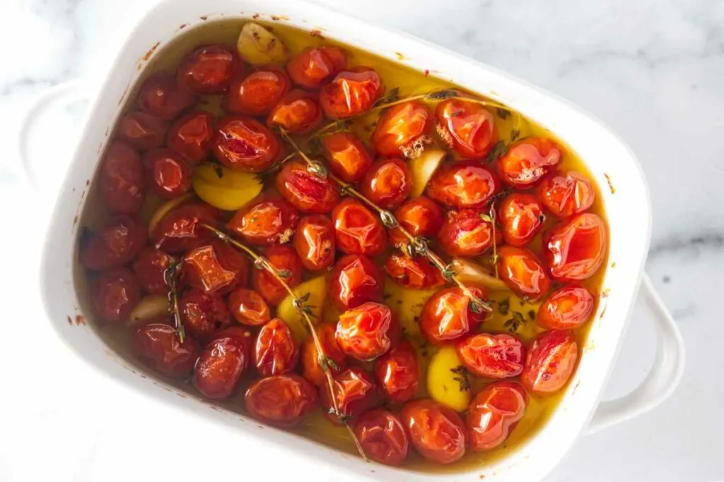 A dish of tomatoes, garlic and thyme sprigs, covered in olive oil.